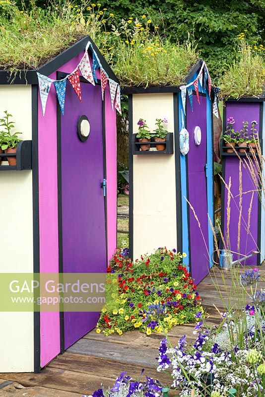 A line of beach huts with wildflower green roof and colourful petunias - Fun On Sea Seaside garden - RHS Hampton Court Palace Flower Show 2017 - Design: Tony Wagstaff