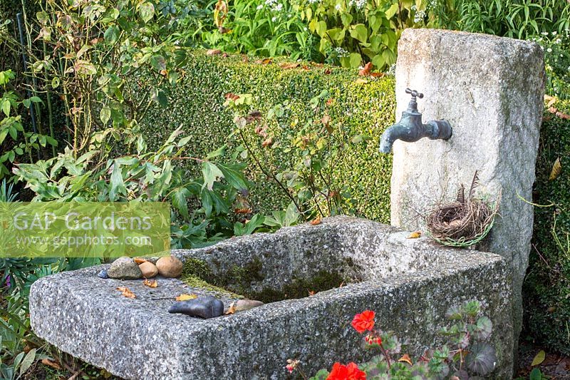 Backed by a clipped hedge, a granite water basin and vertical stone with tap