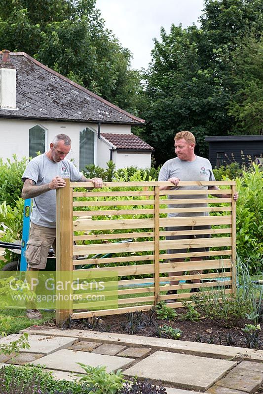 Men using spirit level to ensure post and fencing panel is straight