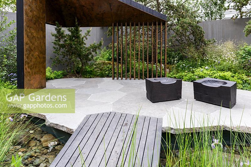Recreation of boreal forests with angular loggia of burnt larch lined with pattinised copper and burnt timber cube seats on granite blocks paving - The Royal Bank of Canada Garden - RHS Chelsea Flower Show 2017 - Designer: Charlotte Harris - Sponsor: RBC