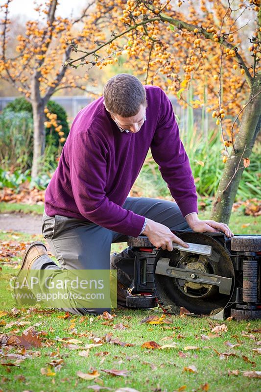 Using a brush to clean dirt and grass off mower blades before winter