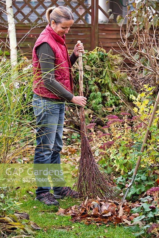 Woman collecting up fallen autumn leaves using a home made birch broom.