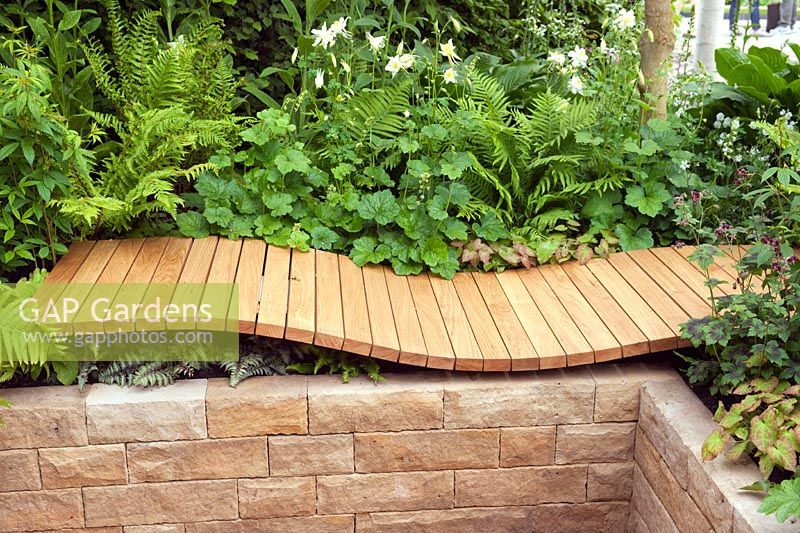 Wooden deck recliner on wall of raised bed with mixed planting, A Celebration of Caravanning, RHS Chelsea 2012.
