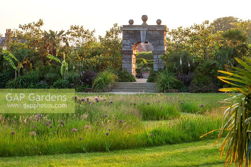Stone arch overlooking Allium and grass meadow at the Collector Earl's Garden, Arundel Castle, West Sussex. 