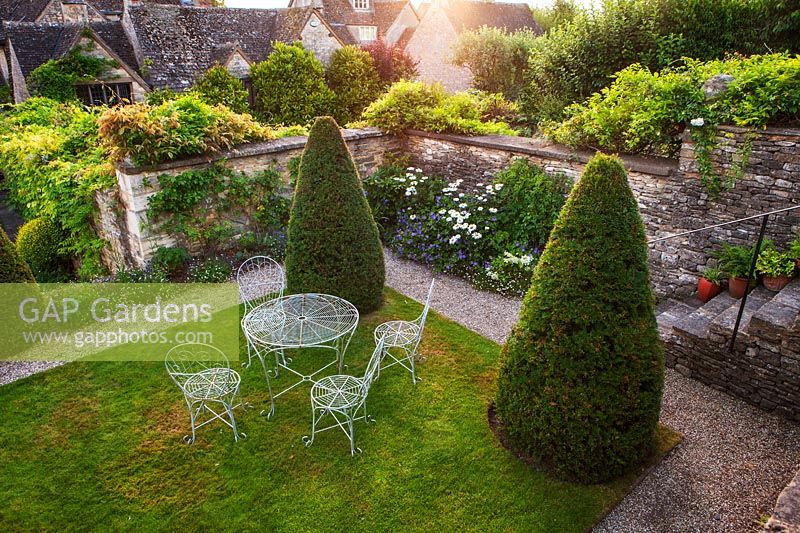 Yew cones on rectangular lawn with garden furniture, Burford, Oxfordshire.