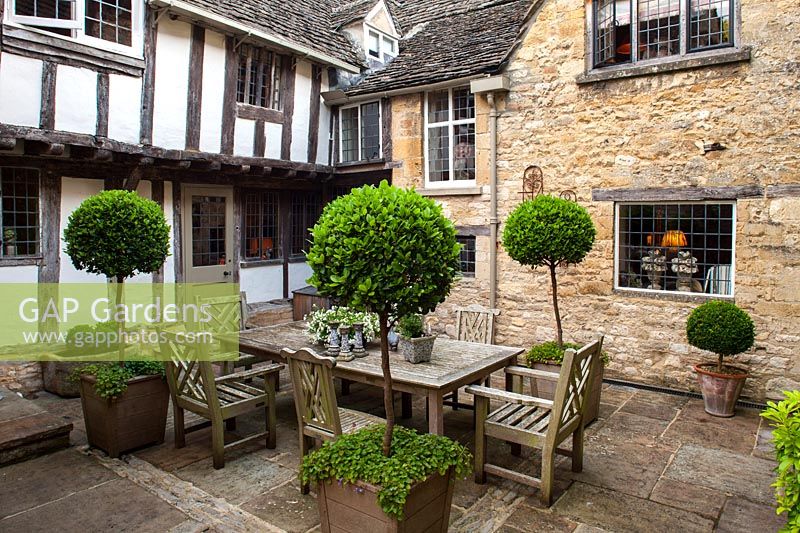 Courtyard garden and outdoor dining area with potted Bay trees, Burford, Oxfordshire.