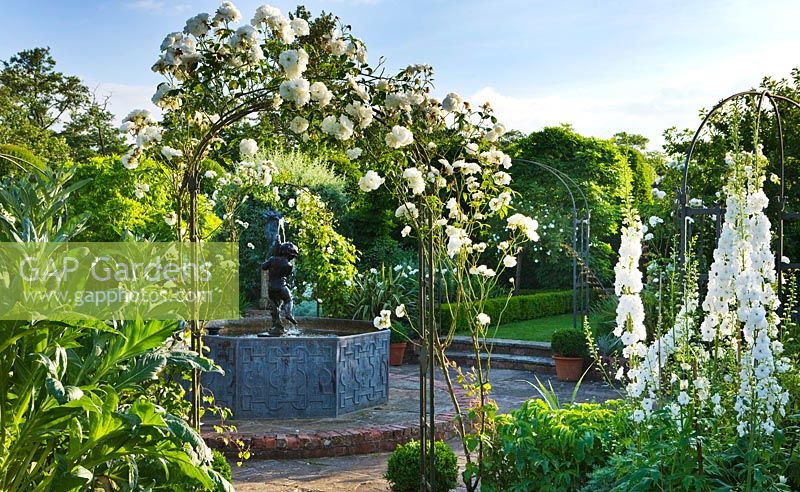 Lead pool with Cherub fountain, white Delphiniums and metal arch with Rose 'Iceberg'