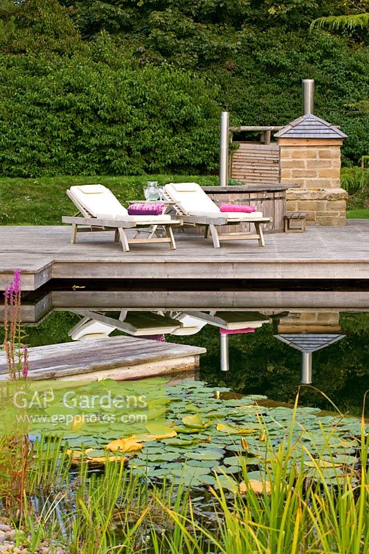 Decking beside 'natural' swimming pool with sun loungers and outdoor oven and barbecue
