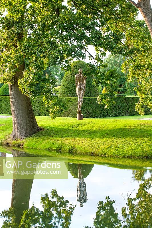 View across water to sculpture in stainless steel set against garden backdrop