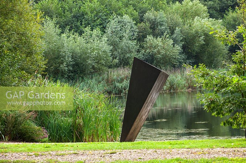 Metal sculpture beside water with green backdrop