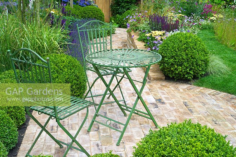 Small wirework table and chairs in a brick paving area of a garden