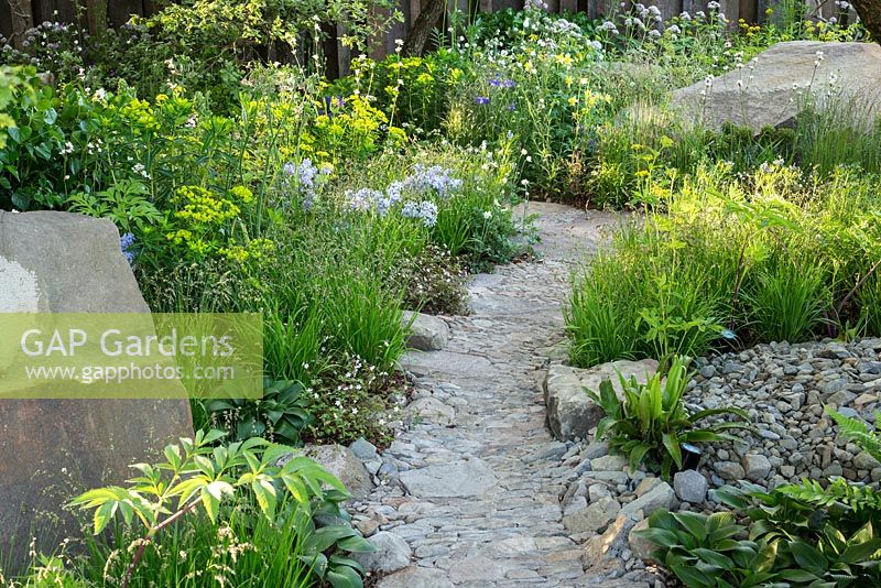 Stone and gravel path with boulders and woodland planting. The M and G Garden, RHS Chelsea Flower Show 2016. Designer Cleve West.