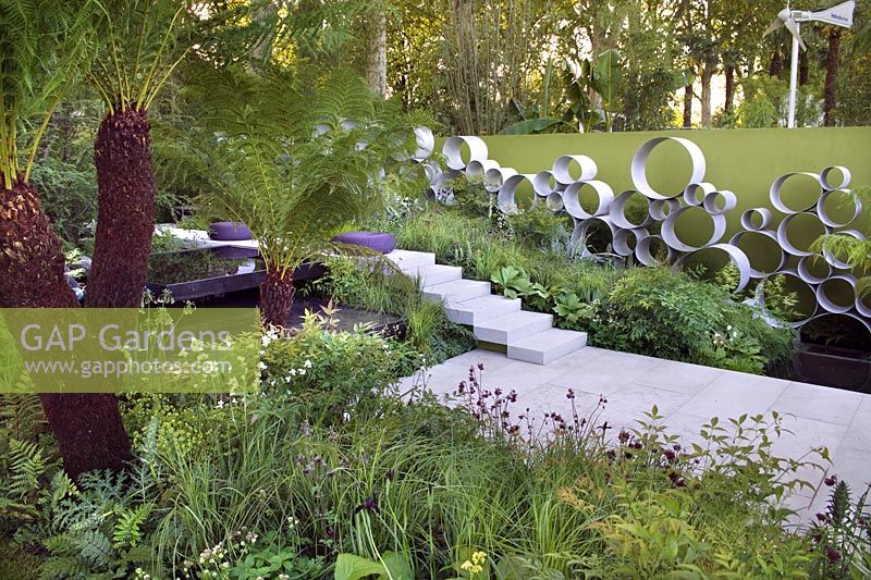 Chelsea Show Garden with water feature, tree fern foliage, perennial planting, wall of steel rings or circles by Andy Sturgeon