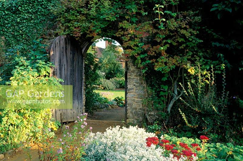Munstead Wood Surrey Gertrude Jekyll Door in stone wall Summer garden with view of house