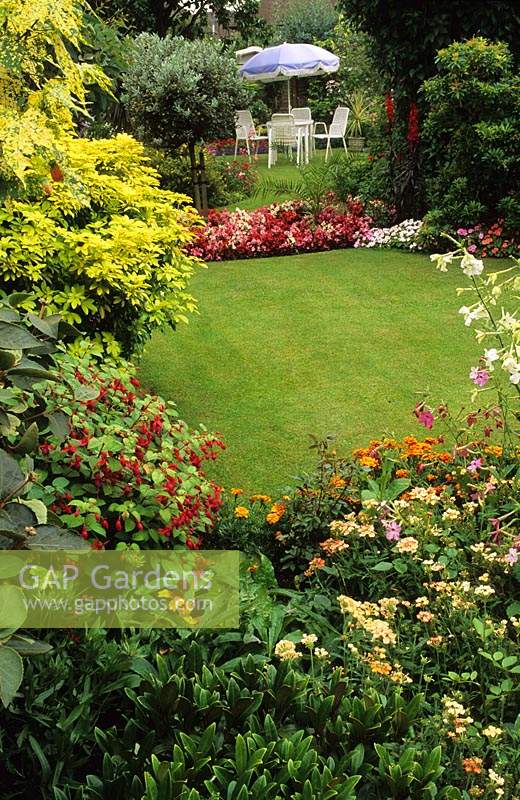 Cornmeadow, Worcestershire. small suburban town garden with lawn surrounded by colourful summer borders and table and chairs