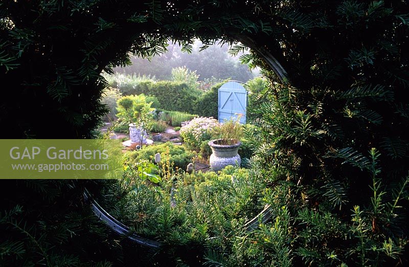 Tilford Cottage Surrey View of formal herb garden through circular window in yew hedge