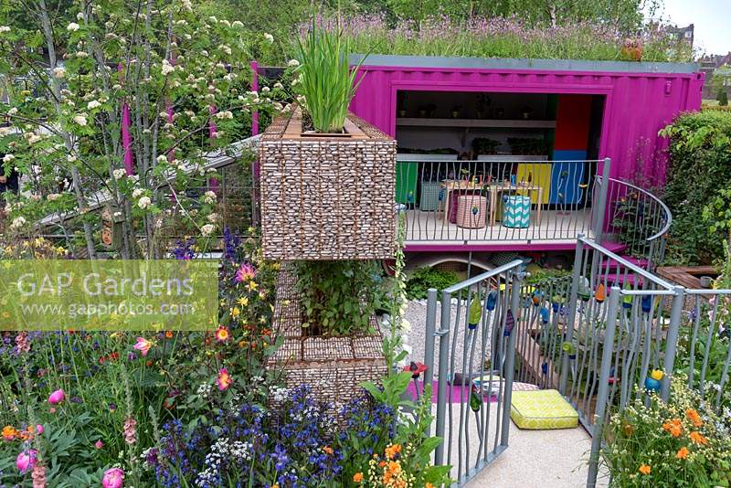 The Montessori Centenary Children's Garden  a view through the gate leading to childrens classroom and play area. Plants include:  Red Campion - Silene dioica growing on the roof,   Designer: Jody Lidgard, Sponsors: Montessori Centre International. RHS Chelsea Flower Show 2019