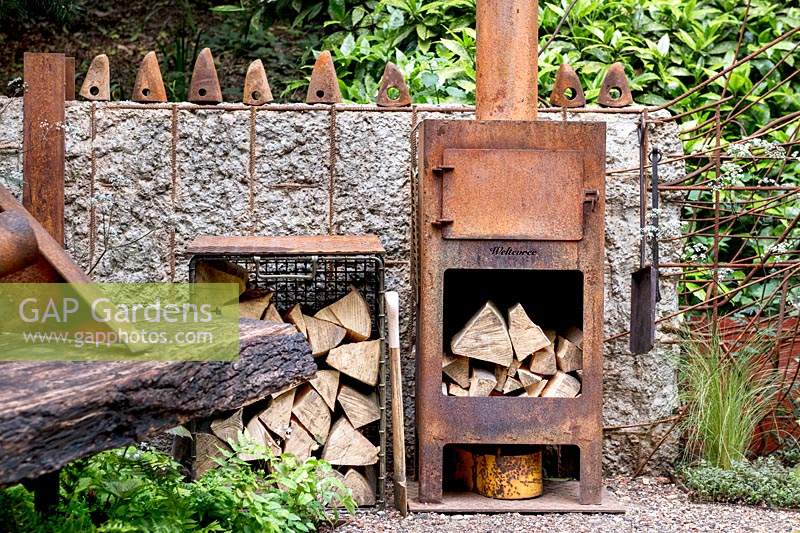 Walker's Forgotten Quarry Garden. Old rusted wood stove and logs. Designer: Graham Bodle. Sponsor: Walker's Nurseries