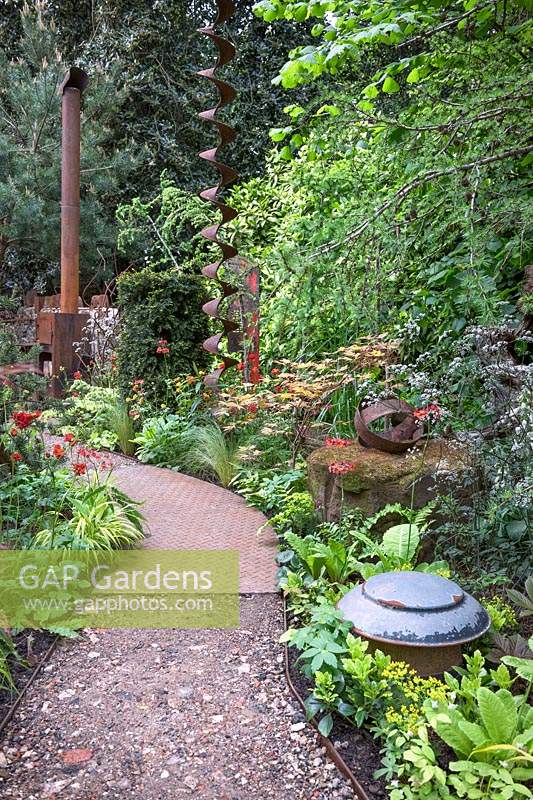 Walker's Forgotten Quarry Garden. Pathway of rusted steel industrial panels leading to wood stove. Planting includes: Geum, Taxus baccata - Yew, Anthriscus sylvestris 'Ravenswing', Stipa tenuissima. Design: Graham Bodle. Sponsor: Walker's Nurseries