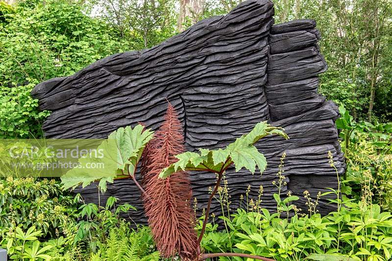 The M and G Garden. Blackened timber sculptures by Johnny Woodford, creating a dramatic backdrop for green woodland planting. Awarded an RHS Gold Medal. Designer: Andy Sturgeon. Sponsor: M and G - Chelsea Flower Show 2019
