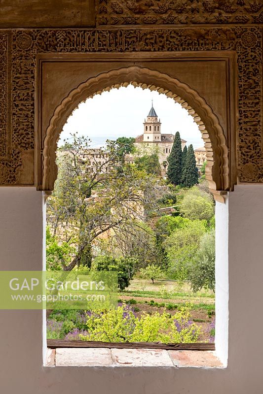 View of gardens and church through ornate stone-carved archway, Generalife Gardens. The Alhambra, Granada.