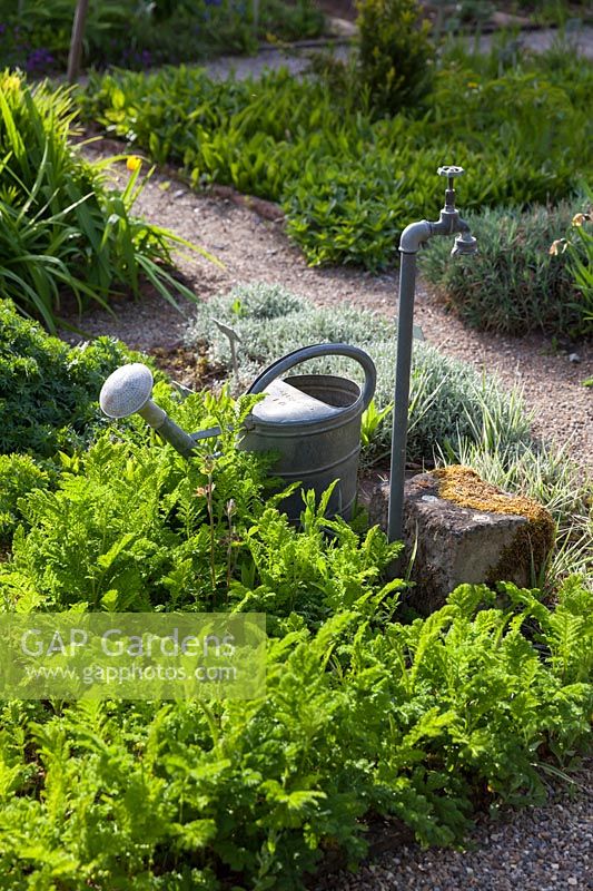 Metal watering can and outdoor tap in gravel garden. 