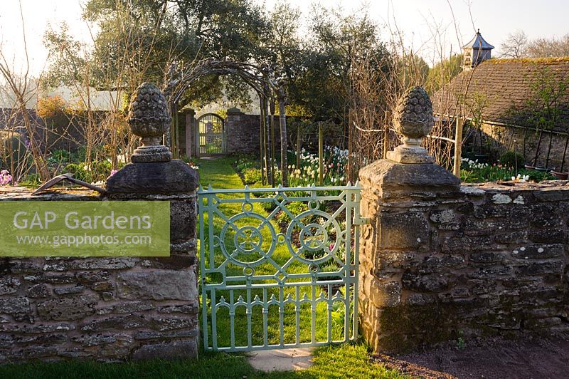 Gate into the cutting garden where a grass path leads beneath four trained whitebeams, Sorbus aria 'Lutescens', down towards a gate into the kitchen garden. Brilley Court Farm, Whitney-on-Wye, Herefordshire