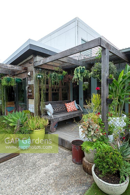 A Timber pergola surrounded by pots of succulents and hanging baskets with an Indonesian timber bench, Australia 