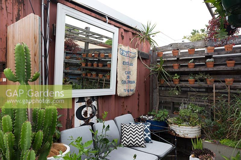 Old timber pallets and converted shipping containers are used to create a relaxed seating area in open air cafe, Australia.
