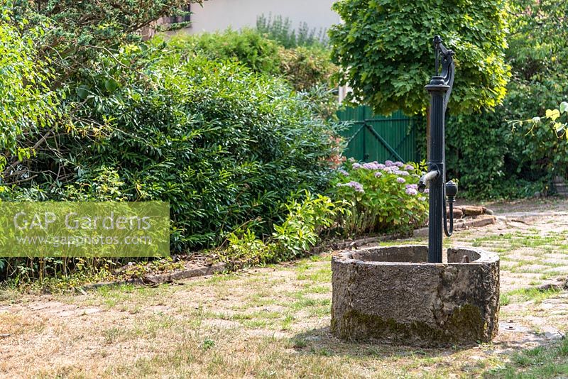 Old well with water pump in a garden. 