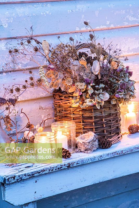Dried seedheads, including hydrangeas, honesty, nigella, wheat and poppies, in a willow basket with tealights