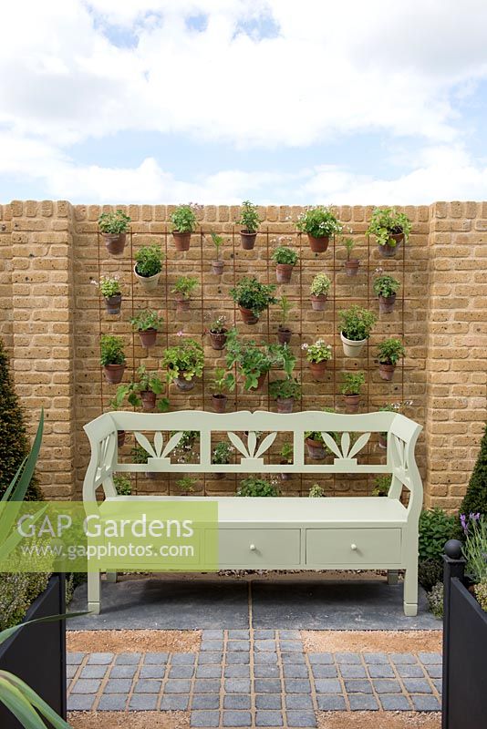 Painted bench in front of a wall with pots hanging on a wire grid - The Perfumer's Garden, RHS Malvern Spring Festival 2018. 