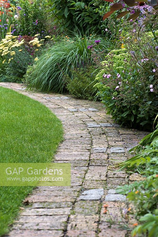 Curving brick path separates lawn from herbaceous border.