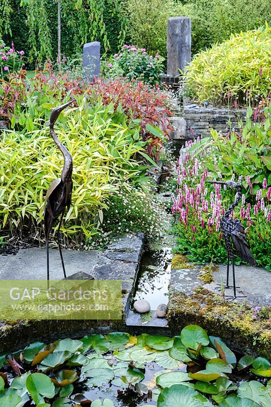 Two metal bird sculptures overlook rill and garden pond, Dipley Mill, Hartley Wintney, Hants, UK. 
