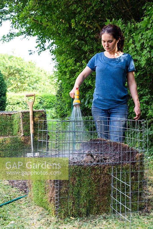 Woman using a hose to soak gabion half filled with topsoil and lined with turf
