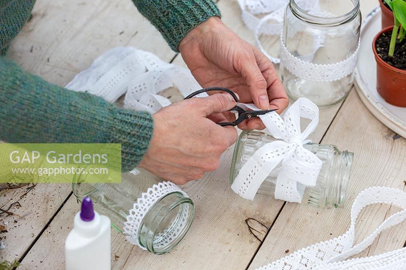 Woman cutting lace ribbon to finish off bow tied around jam jar