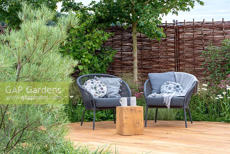 Willow woven fence with chairs on oak decking, Salix rosmarinifolia in foreground and Corylus avellana and Acer campestre behind - Raised by Rivers, RHS Tatton Park Flower Show 2018