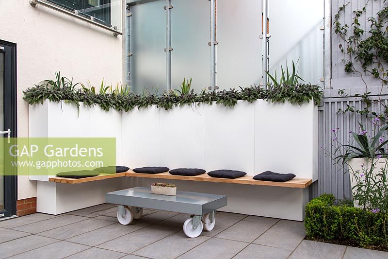 Simple bench with cusions and table on wheels, in modern courtyard garden.