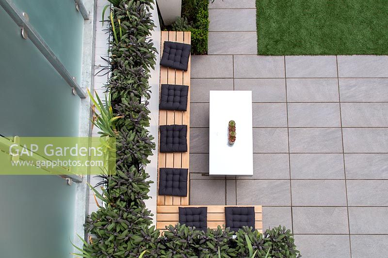 View from above to simple bench with cusions and table in modern courtyard garden.