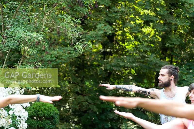 Yoga in a green garden. 4 people are in the position Virabhadrasana II