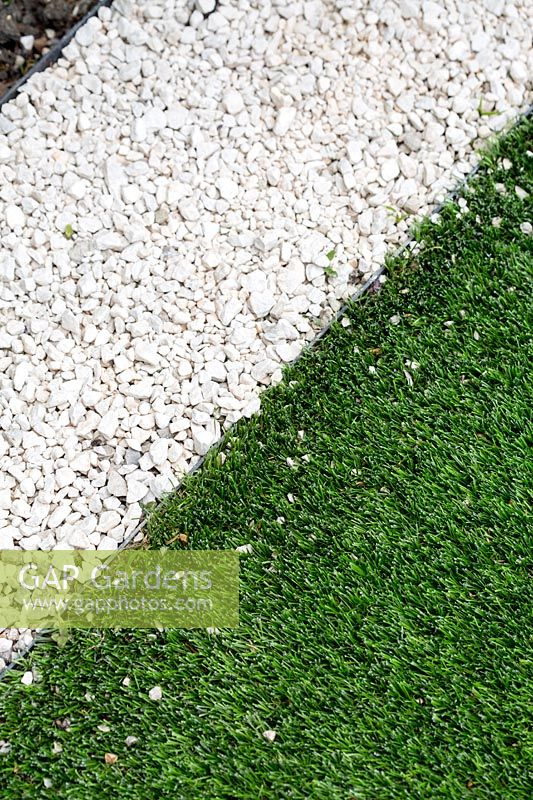 Close up of artificial lawn edge with white gravel path.