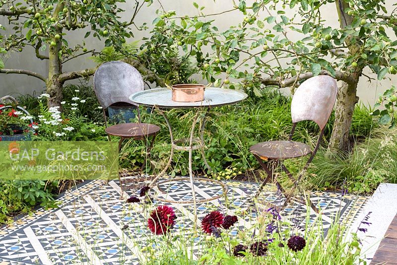 Table and chairs on mosaic tiled patio. 'Style and Design Garden', RHS Hampton Flower Show 2018