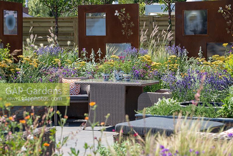 Outdoor Rattan dining furniture surrounded by colourful planting  - RNIB's Community Garden, RHS Hampton Court Palace Flower Show 2018