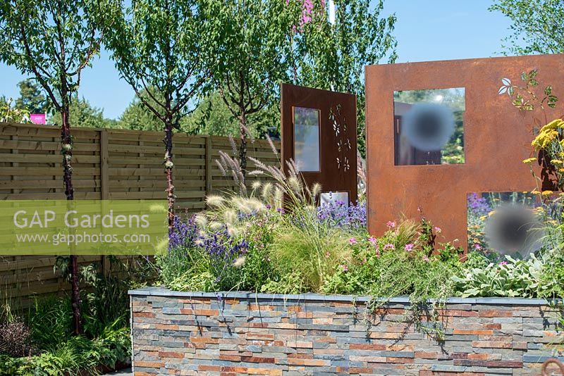 Fence with row of Prunus serrula, raised bed with tile feature and steel decorative panels by Steel Project Management - RNIB's Community Garden, RHS Hampton Court Palace Flower Show 2018