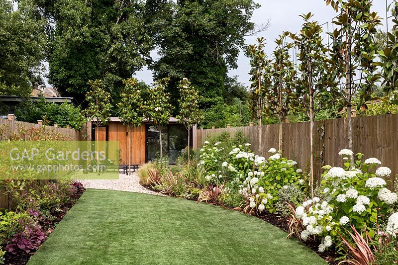 General view of garden with artificial lawn, including borders, looking towards garden room and patio area. Contemporary garden in Dulwich 