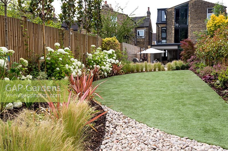 View down modern garden with artificial grass and flowering shrubs. 