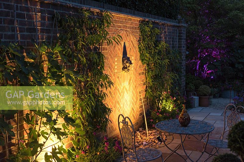 A small walled courtyard and seating area with illuminated water feature.