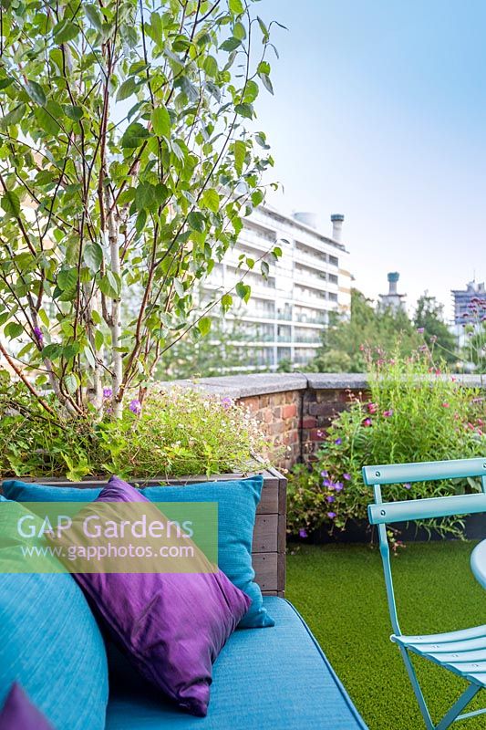 In built garden bench with blue and purple cushions on small urban roof terrace, London, Uk. 