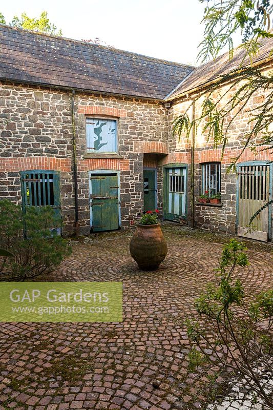 Central Greek terracotta pot in paved courtyard, Plaz Metaxu Garden, Devon, UK. 