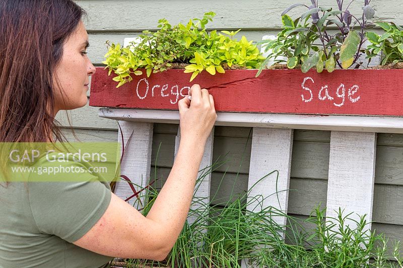 Writing name of herbs on front of pallet planter with chalk.